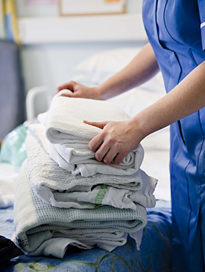Healthcare worker folding clean sheets in a hospital room